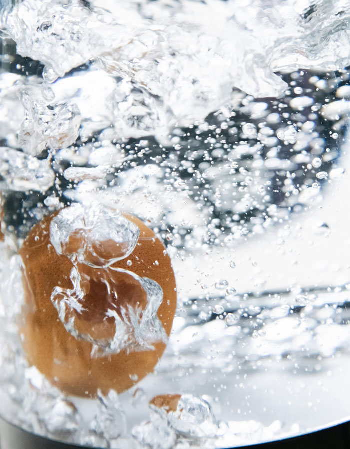 Egg being submerged in water with bubbles illustrating a classic old wives' tale kitchen trick.