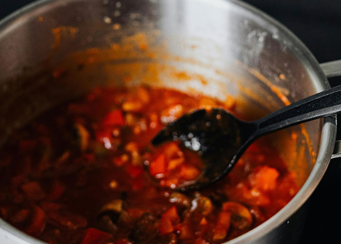 Pot of simmering tomato-based stew with vegetables and a black ladle, related to buffet workers' wildest encounters.