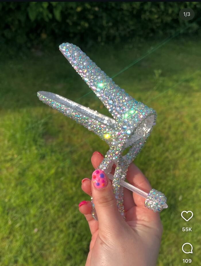 Hand holding a jeweled craft tool covered in sparkling rhinestones against a blurred green background.