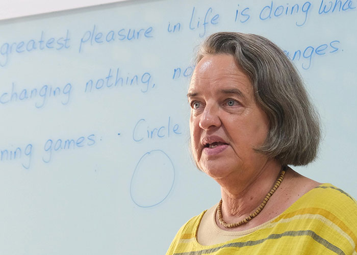 Middle-aged woman speaking near whiteboard, illustrating team moments in a classroom setting for take one for the team discussion.