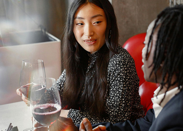 Two people on an awkward date at a restaurant holding wine glasses, with tense expressions during the conversation.