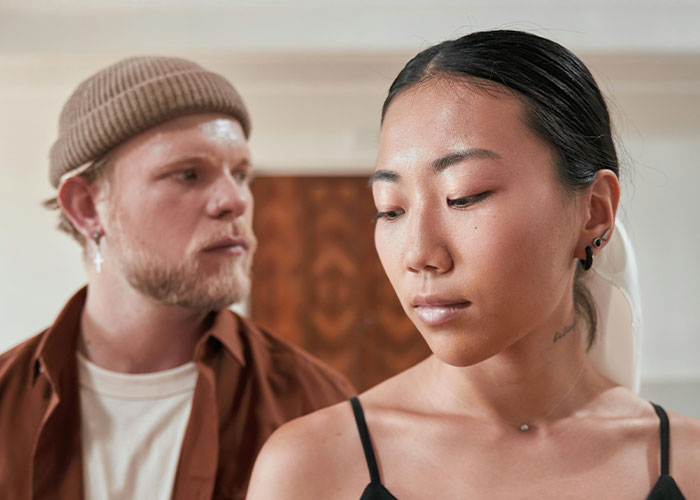 A conflicted couple indoors, woman looking away thoughtfully while man behind her appears concerned, reflecting broken engagements.