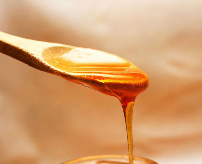 Close-up of honey dripping from a wooden spoon, illustrating a natural remedy in old wives' tales.
