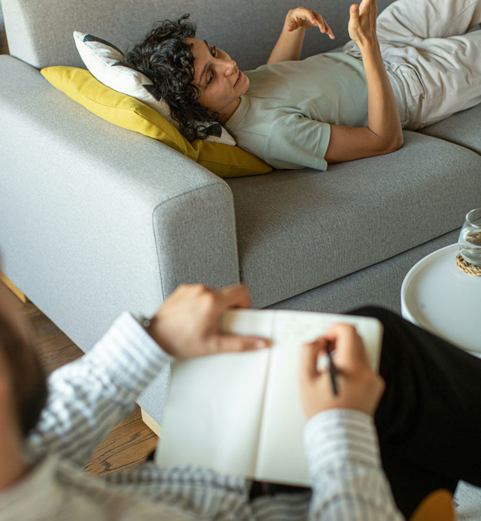 Person lying on couch sharing insane therapy revelations with therapist taking notes during session indoors