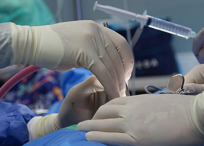 Gloved hands of medical professionals performing a procedure inside the birthing room with surgical instruments in use.