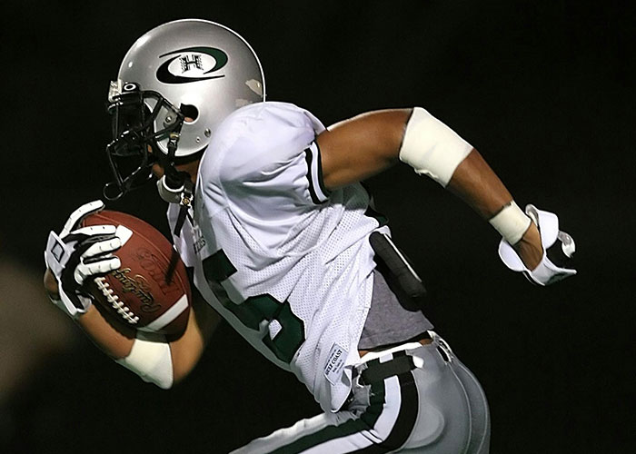 Football player in white uniform running with the ball, showcasing a big take one for the team moment during a night game.