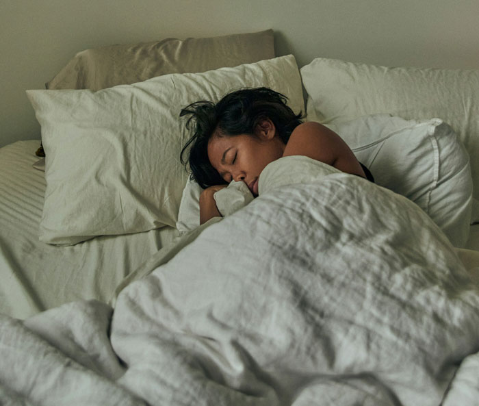Person sleeping peacefully in a bed with white sheets, illustrating wild things people say they’ve seen but no one believes.