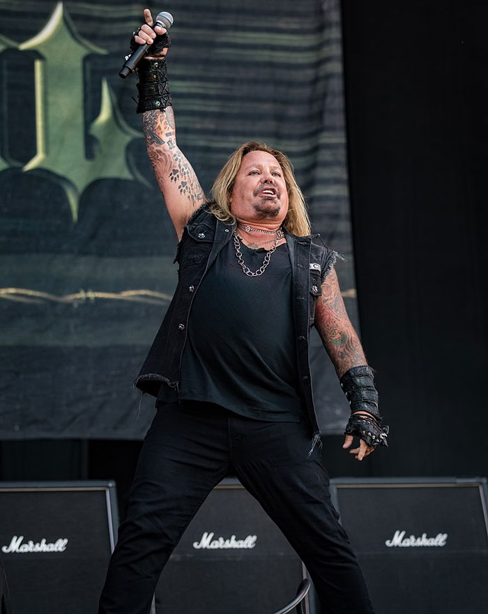 Rock musician with tattoos and chains performing on stage, representing famous people who did evil things in the past.