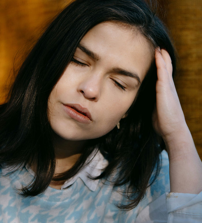 Young woman with eyes closed and hand on head, expressing regret and reflecting on biggest life mistakes.
