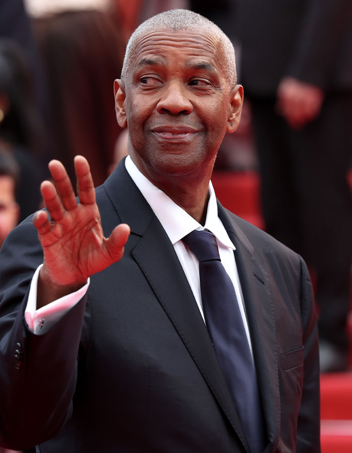 Celebrities who look way younger waving and dressed in a black suit with white shirt on a red carpet event.