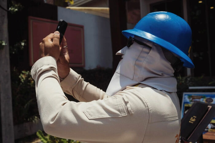 Man in a blue helmet taking a candid street photo with a smartphone, showcasing urban life in a candid street photo style