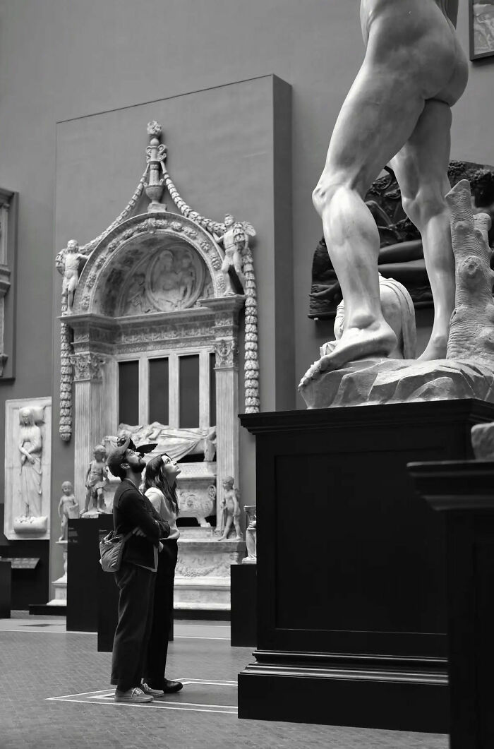 Couple observing large classical statue in museum, illustrating beautiful street shots capturing the poetry of everyday life.