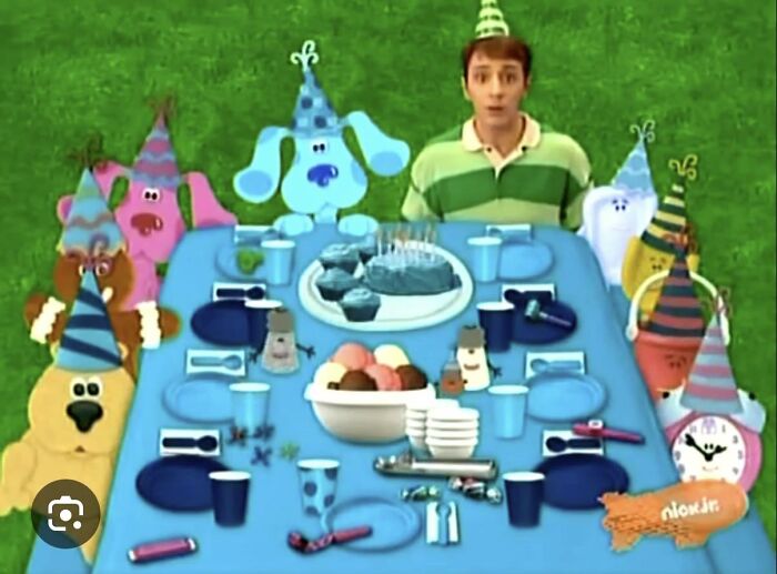 Scene from Blue's Clues party with Steve and animated characters wearing party hats around a table with cake and snacks.