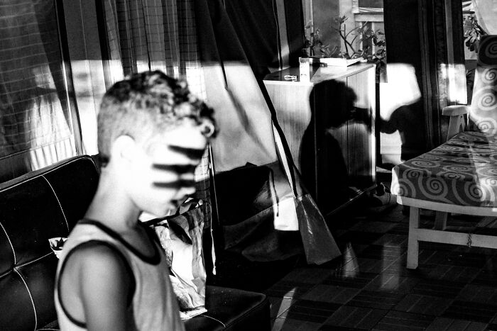 Black and white perfectly-timed street photo showing a boy with shadows on his face and a silhouette on the wall behind him.