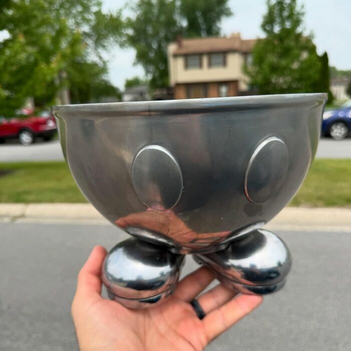 Hand holding a vintage metal bowl with round feet, representing cool secondhand finds in an outdoor setting.