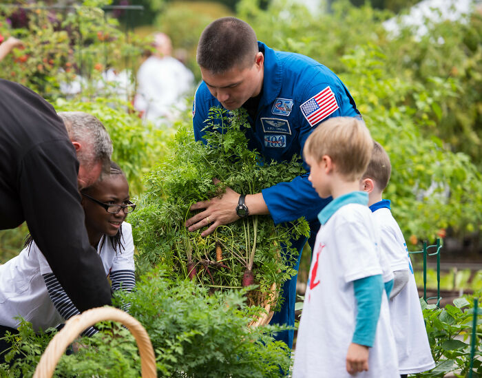 Astronaut in blue suit teaching children about gardening outdoors, highlighting intriguing and bizarre astronaut facts.