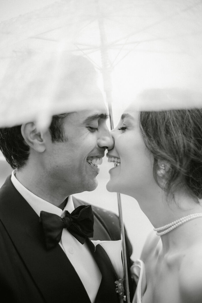 Close-up black and white wedding photo of a smiling couple under an umbrella sharing an intimate moment.