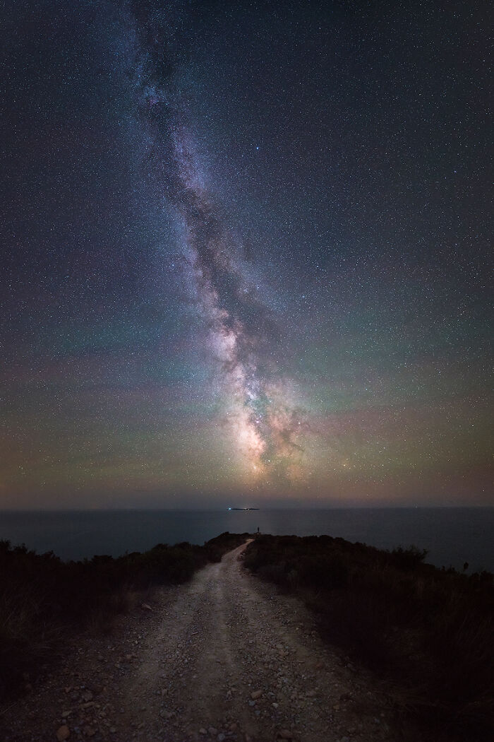 Milky Way galaxy over a coastal dirt path at night showcasing breathtaking travel photography by the Bored Panda community.