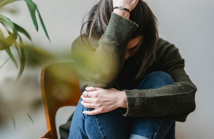 Woman sitting on a chair feeling distressed and grossed out, covering her face with her hand, wearing casual clothes. Woman sitting on a chair feeling distressed and grossed out, covering her face with her hand, wearing casual clothes.