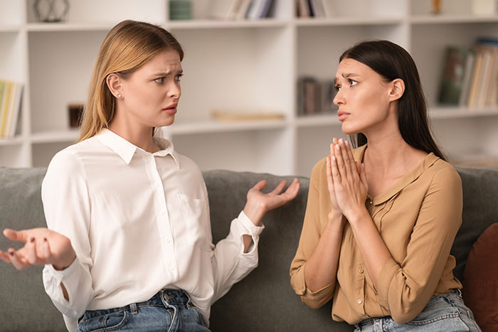 Two women having a tense conversation on a couch, one appearing frustrated while the other pleads for help. Two women having a tense conversation on a couch, one appearing frustrated while the other pleads for help.