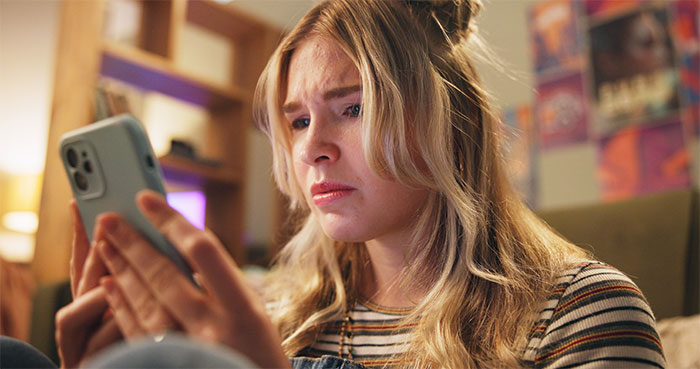 Woman looking upset at her phone, reflecting conflict over surrogacy and family baby plans.