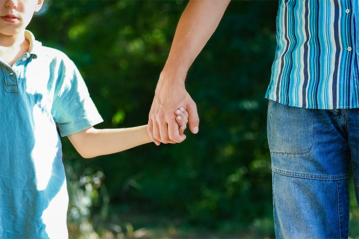 Father and child holding hands outdoors, symbolizing a dad active in kids&rsquo; life despite challenges with ex&rsquo;s new husband.