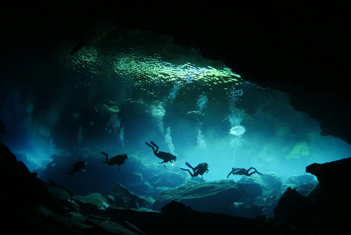 Scuba divers exploring one of the scariest places around the world in a dark underwater cave system.
