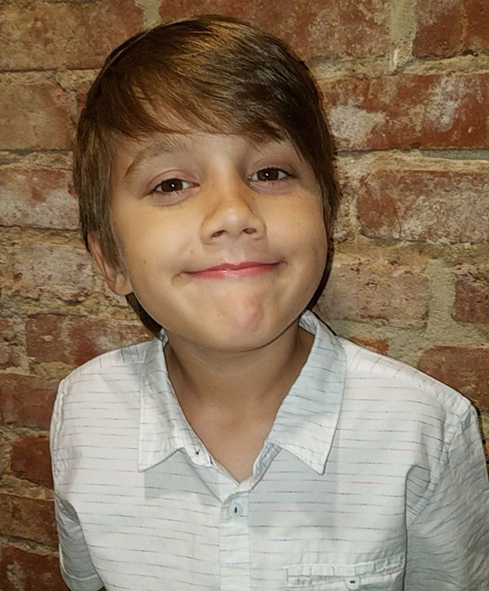 Young boy smiling softly in a white shirt against a brick wall, related to 16 and Pregnant star Whitney Purvis news.