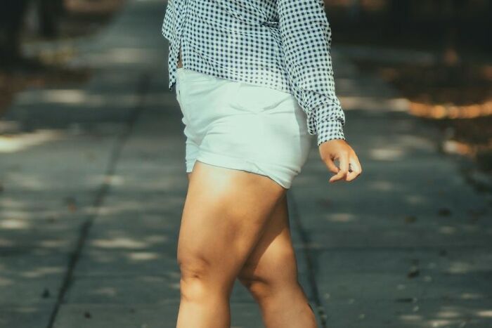 Woman over 40 wearing white shorts and a checkered shirt walking outdoors, symbolizing confidence and self-acceptance.