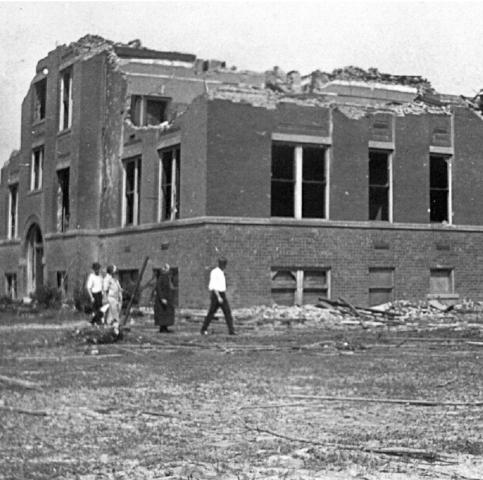 Damaged building and people walking through debris after the worst tornado in US history with 695 lives lost.