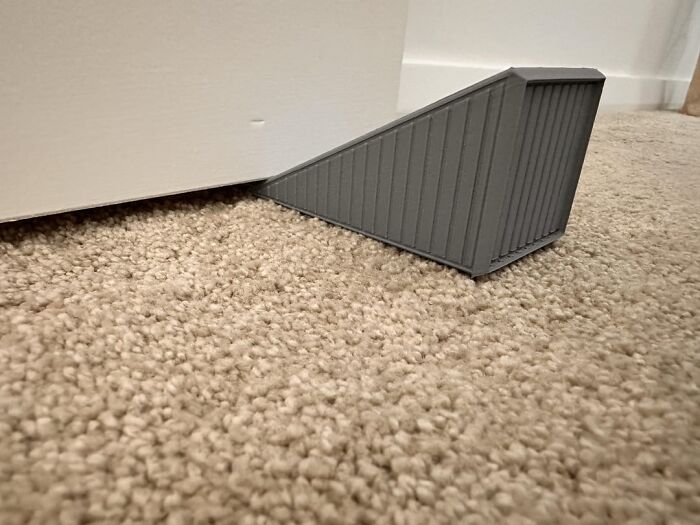 Gray door stopper wedge placed on carpet floor to prevent door movement, illustrating uncommon hacks for women living alone.