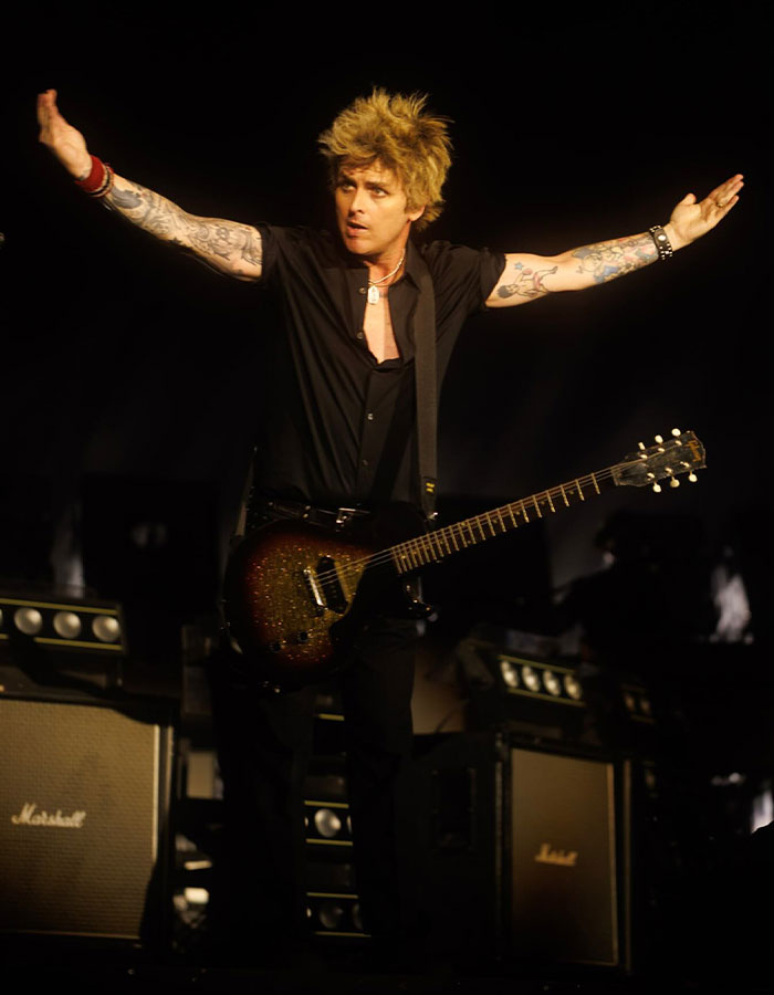 Billie Joe Armstrong of Green Day on stage with arms outstretched, holding guitar during a live concert performance.