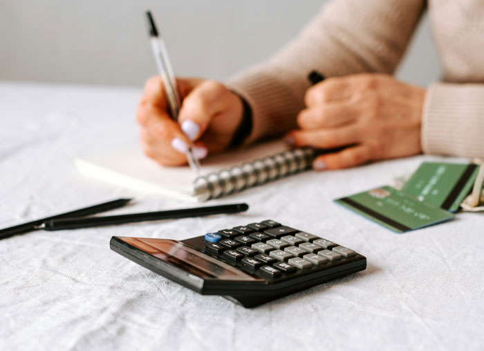 Person using a calculator and writing in a notebook with credit cards nearby representing millennials financial planning.