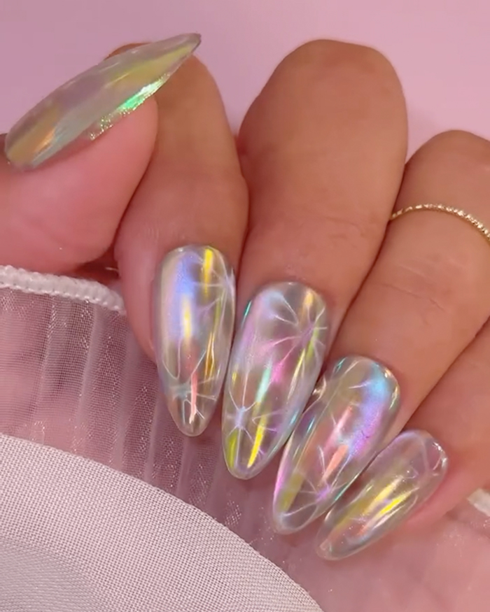 Iridescent and holographic summer nails with delicate white floral designs on long almond-shaped nails.