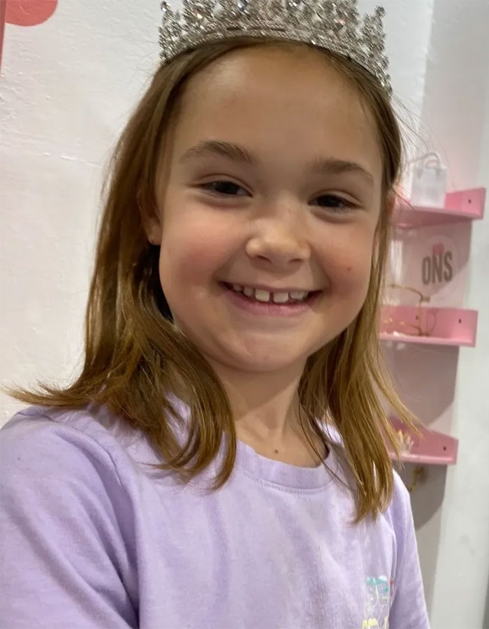 Young girl wearing a tiara and purple shirt, smiling indoors, related to tragic cause of passing of 3 sisters after visitation.