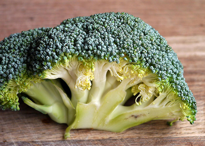 Close-up of fresh broccoli on a wooden surface, highlighting texture and color in natural lighting.