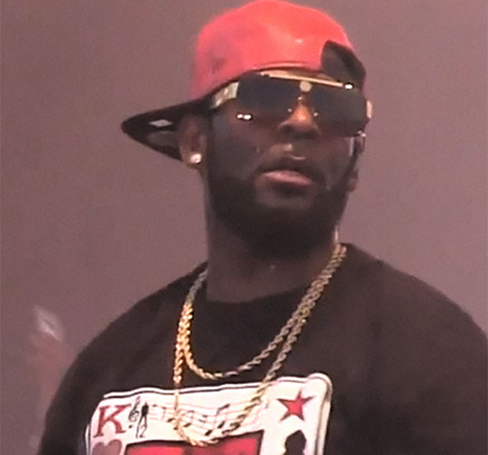 Man wearing red cap backwards, dark sunglasses, and gold chains, representing famous people who did evil things in the past