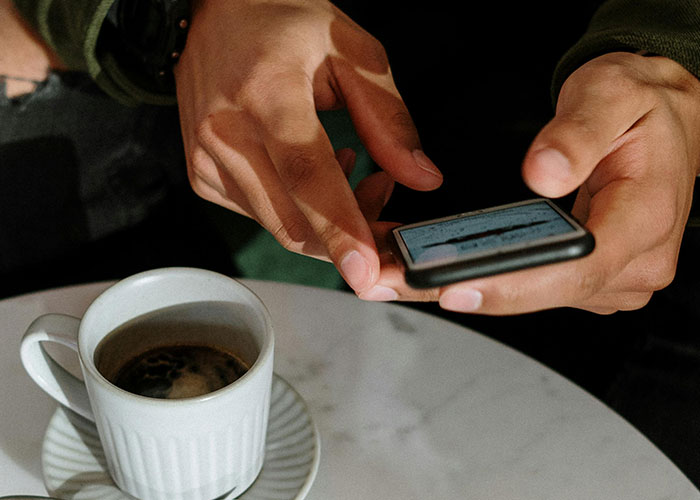 Person holding a smartphone over a table with coffee, capturing a moment from an awkward date experience.