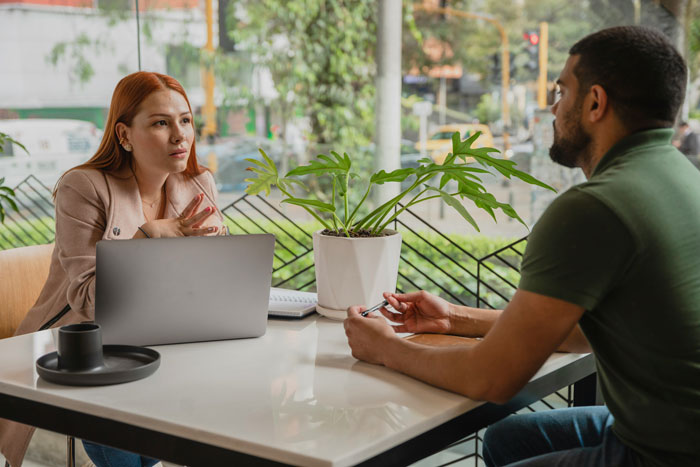Woman and man in therapy session discussing insights and personal revelations in a bright indoor setting with a laptop and plant on table
