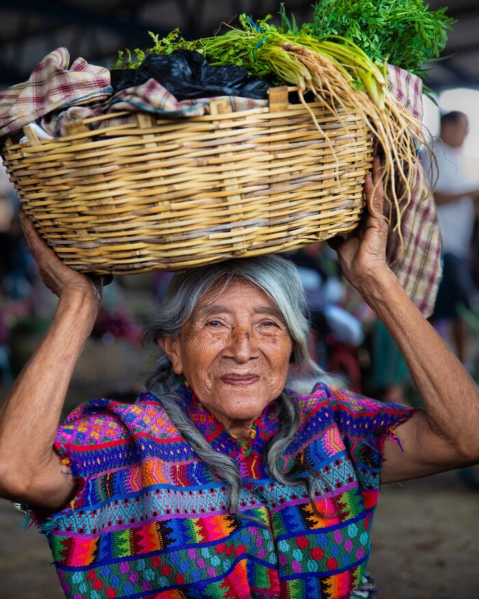 Elderly woman from around the world smiling while carrying a basket on her head, showcasing timeless beauty and culture.