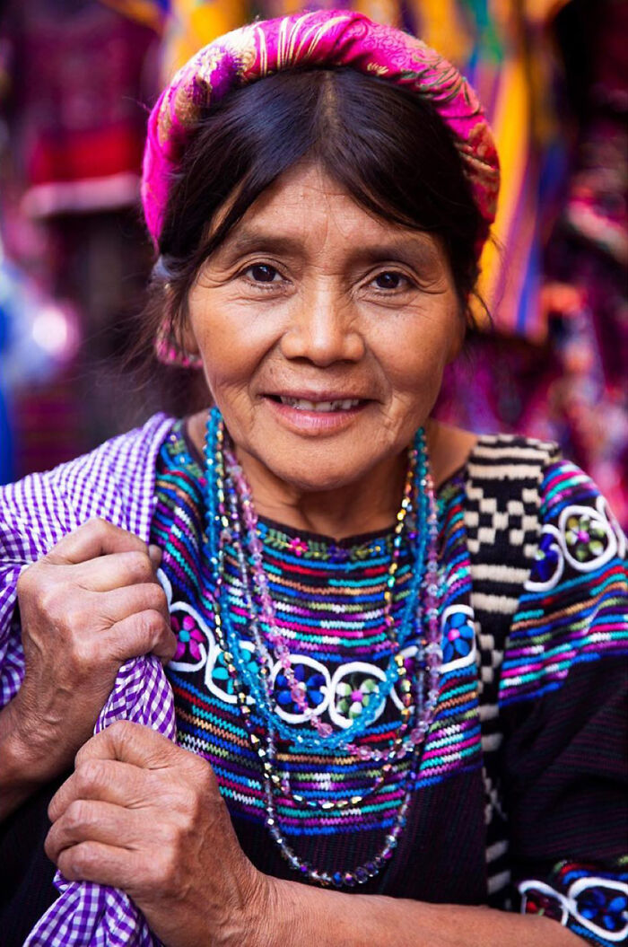 Elderly woman wearing colorful traditional clothing and beaded necklaces, smiling warmly, showcasing beauty without expiration.