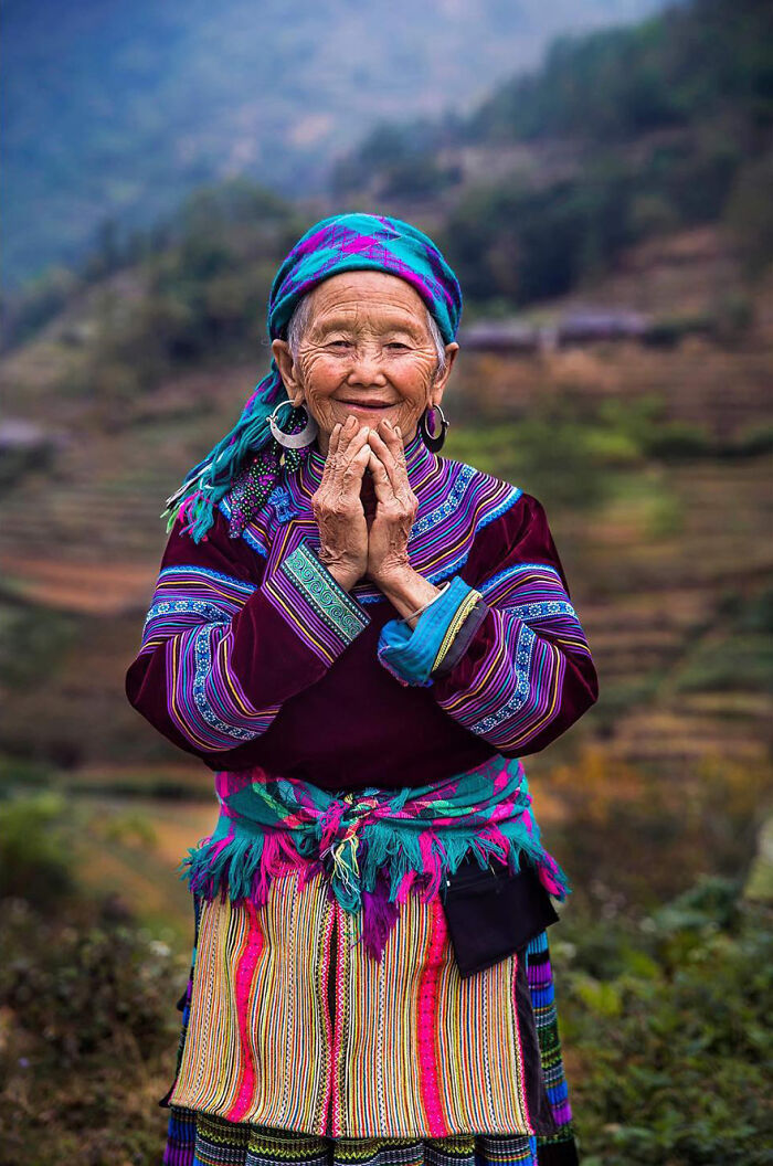 Elderly woman wearing colorful traditional clothes smiling outdoors, showcasing beauty and cultural heritage.