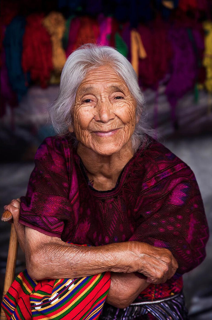 Elderly woman with white hair smiling warmly, wearing traditional colorful clothing, showcasing timeless beauty and grace.