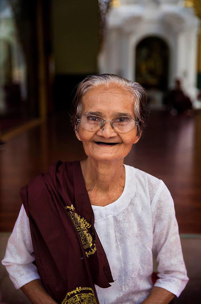 Elderly woman from Asia smiling, wearing glasses and traditional clothing, showcasing beauty and age gracefully.