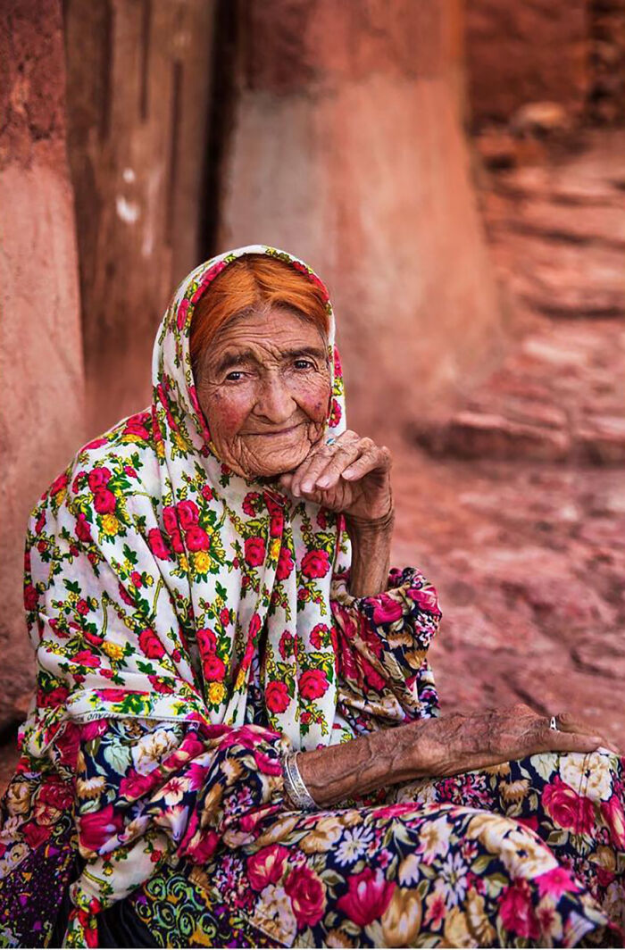 Elderly woman wearing a colorful floral headscarf and dress, showcasing beauty and grace from around the world.