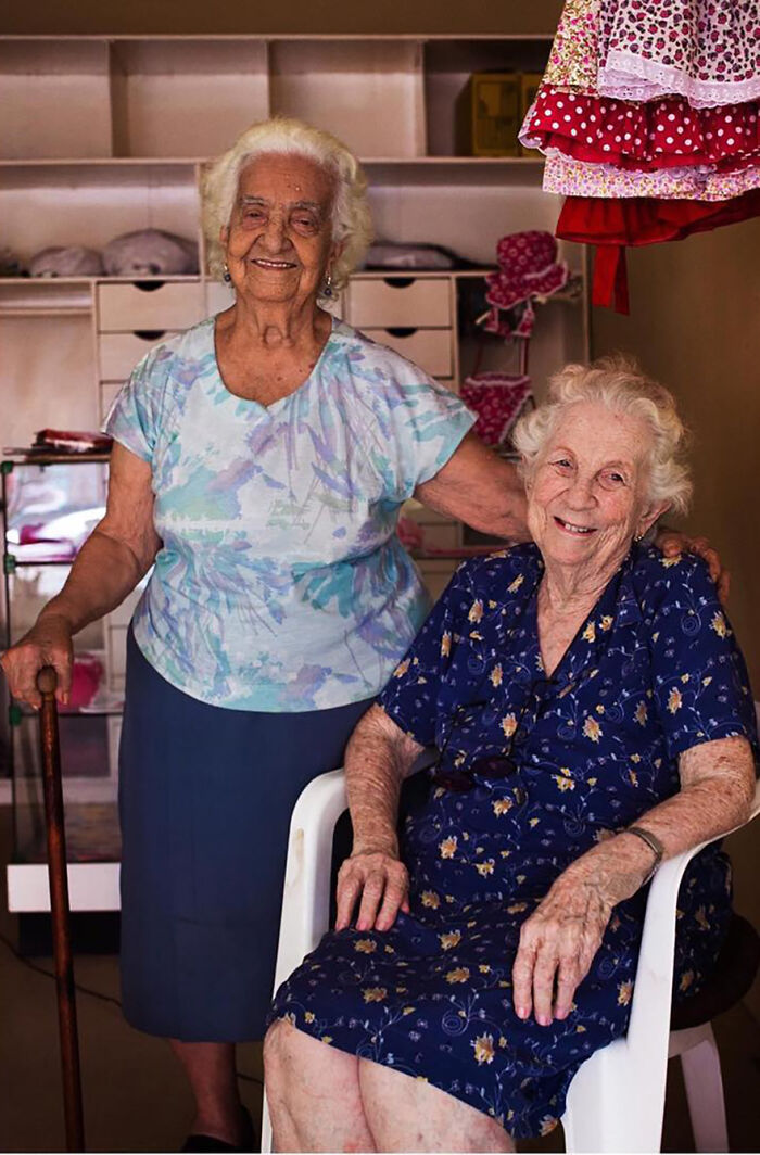 Two elderly women smiling together indoors, showcasing the timeless beauty of elderly women from around the world.
