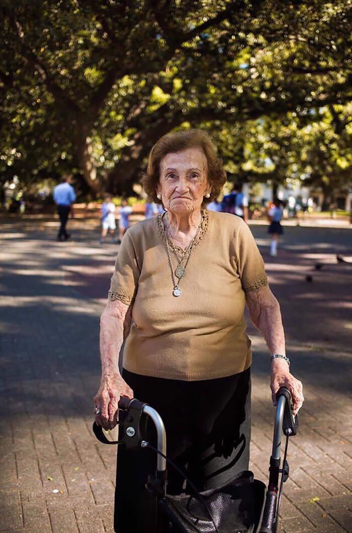 Elderly woman using a walker outdoors in a park, showcasing beauty and strength in aging.