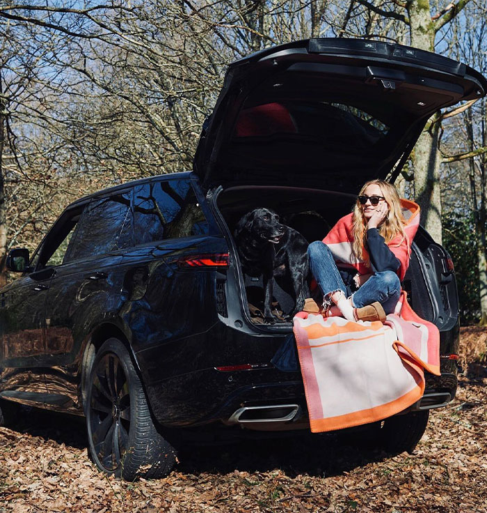 Woman sitting in open car trunk with dog in forest, representing stars who said goodbye to US and Hollywood abroad.
