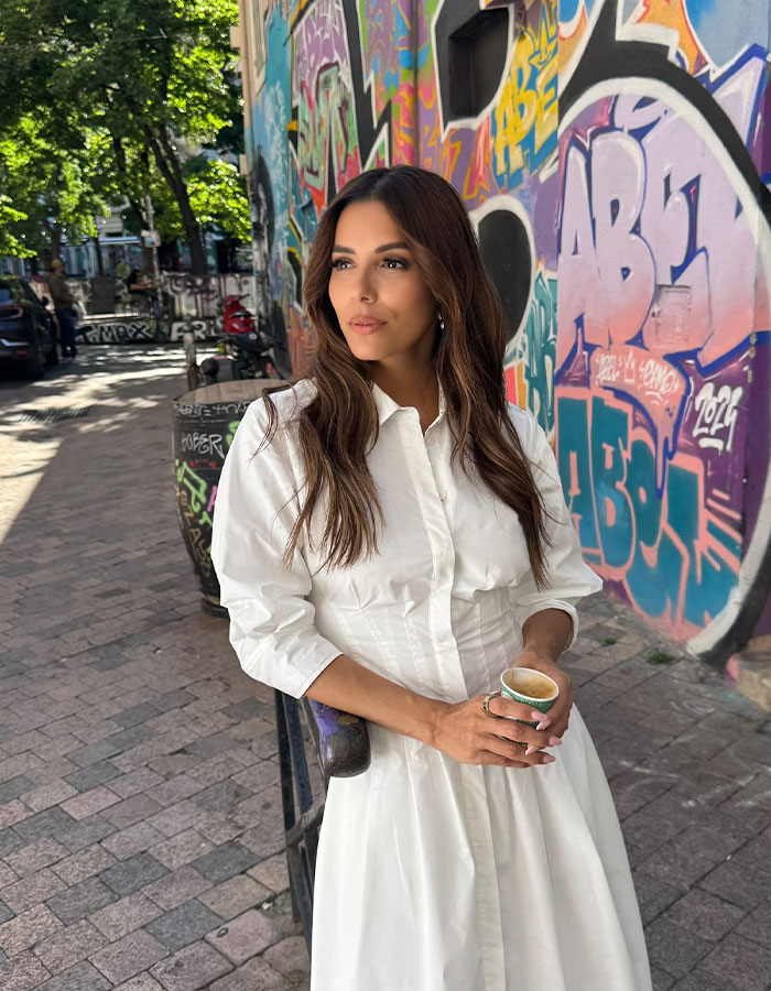 Woman in white dress holding coffee, standing by colorful graffiti wall, representing stars who found new home abroad.