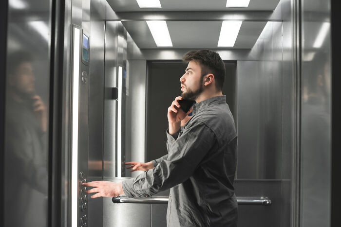 Young man in an elevator speaking on the phone with a serious expression, embodying a completely legal total psychopath mood.